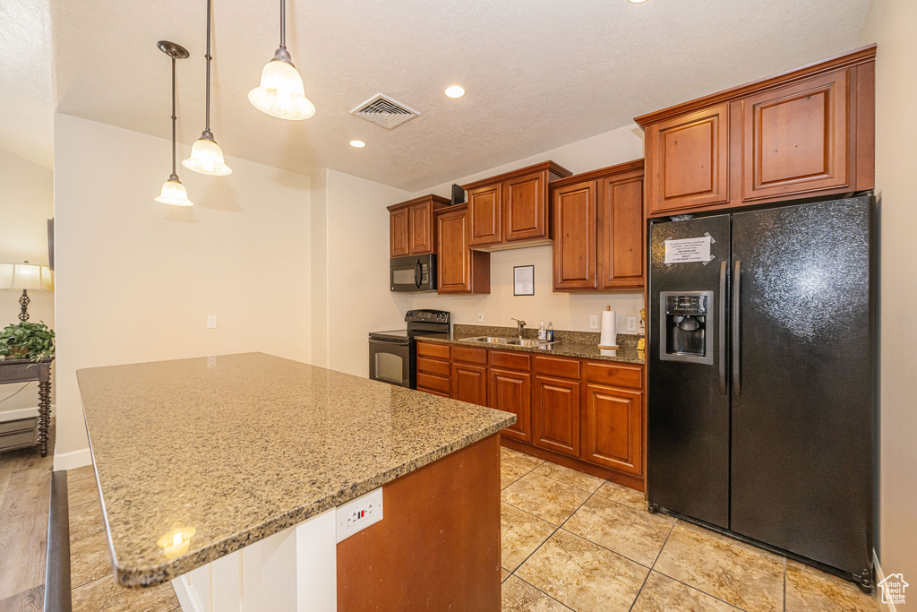 Kitchen with visible vents, light stone countertops, a sink, black appliances, and brown cabinetry