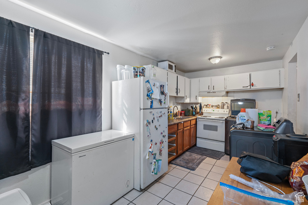 Kitchen with light tile patterned flooring, light countertops, a sink, under cabinet range hood, and white appliances