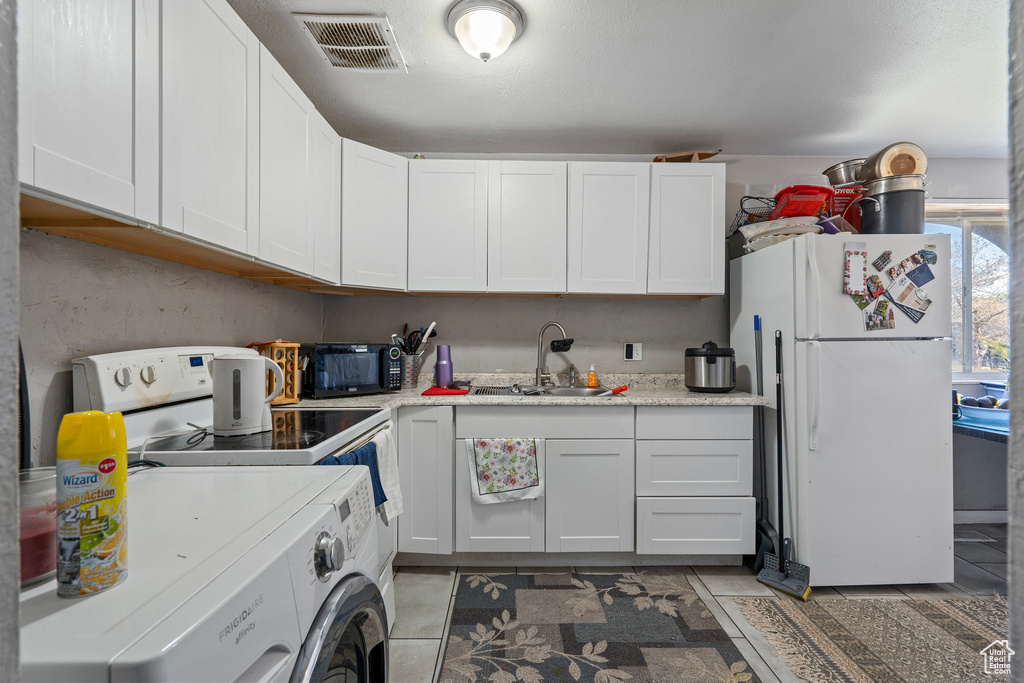 Kitchen with light countertops, a sink, washer / dryer, white appliances, and visible vents