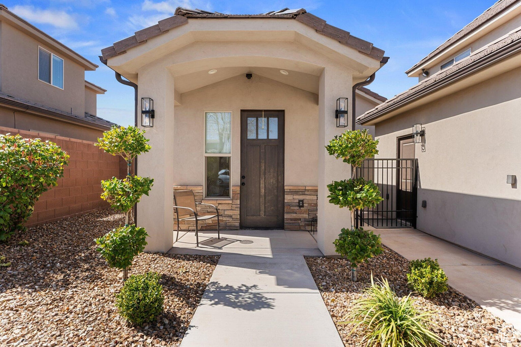 Entrance to property featuring stone siding, stucco siding, and fence