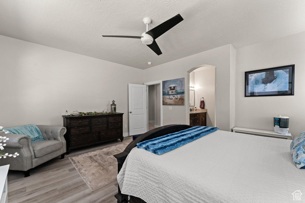 Bedroom featuring a textured ceiling, light wood-style flooring, ceiling fan, arched walkways, and ensuite bath
