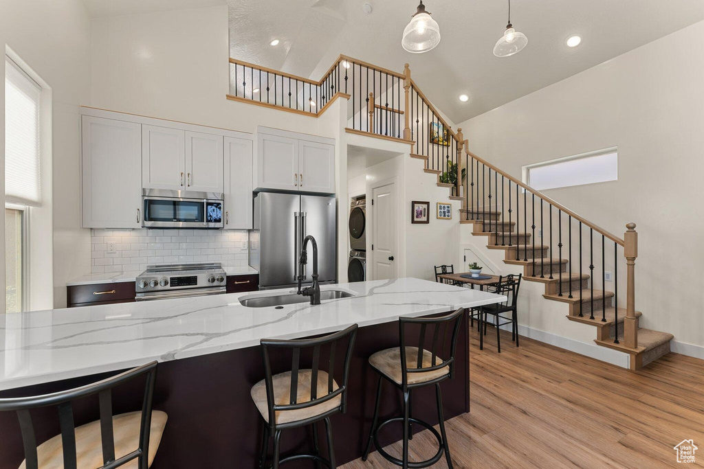 Kitchen featuring stacked washer and clothes dryer, a breakfast bar, stainless steel appliances, a sink, and light wood-type flooring