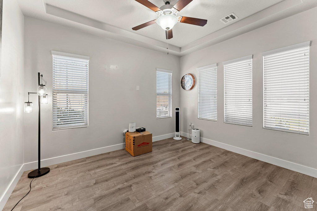 Unfurnished room with a raised ceiling, light wood-style floors, ceiling fan, and visible vents