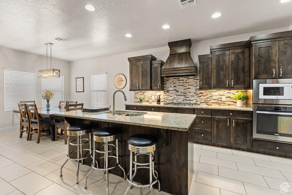 Kitchen with a breakfast bar area, stainless steel appliances, a sink, visible vents, and custom exhaust hood