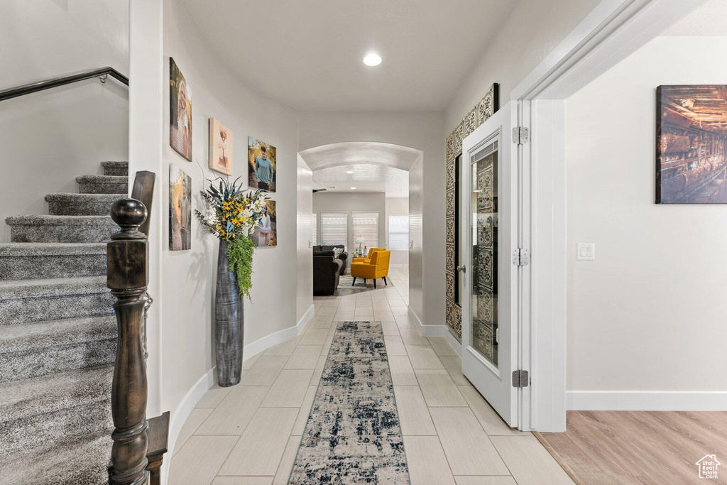 Hall with arched walkways, baseboards, stairs, and recessed lighting