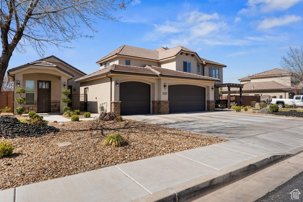 View of front of home featuring stone siding, a gate, fence, concrete driveway, and stucco siding