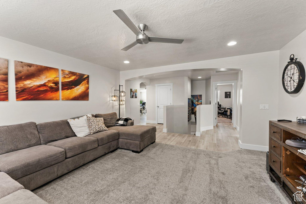 Living room with recessed lighting, a textured ceiling, arched walkways, a ceiling fan, and light carpet