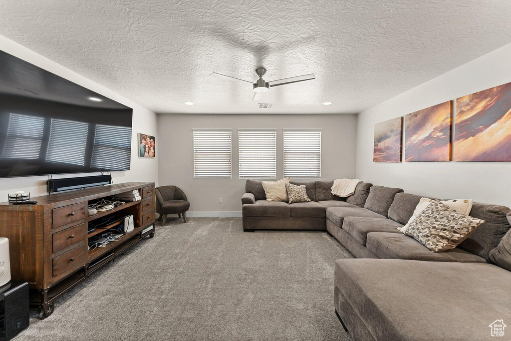 Carpeted living room featuring visible vents, a textured ceiling, baseboards, and ceiling fan