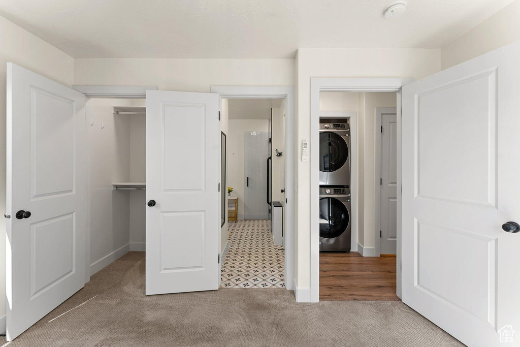Unfurnished bedroom featuring a closet, stacked washer / drying machine, and carpet flooring