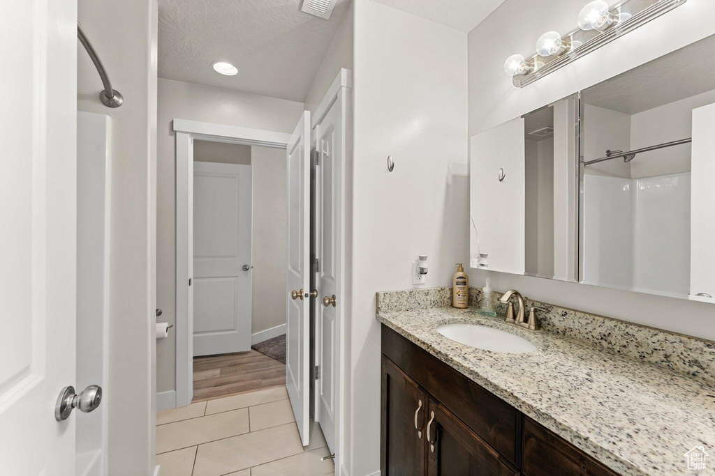 Bathroom with a textured ceiling, a shower, baseboards, vanity, and tile patterned flooring