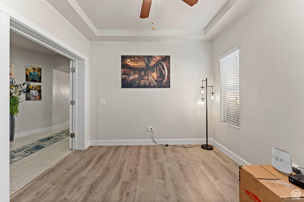 Unfurnished room with ceiling fan, light wood-style flooring, and a raised ceiling