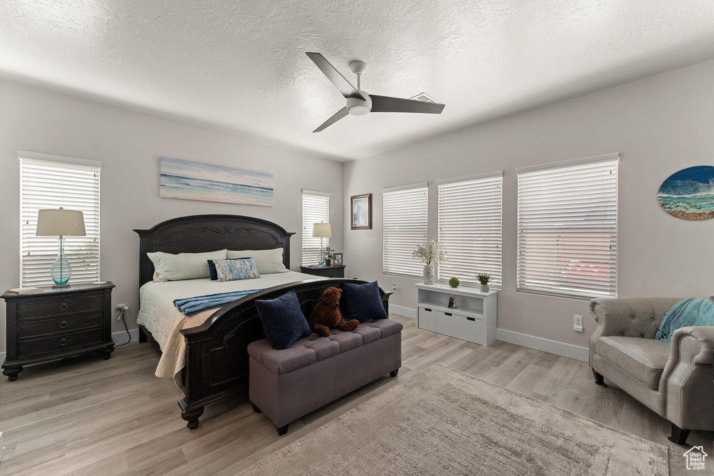 Bedroom with a ceiling fan, light wood-style flooring, baseboards, and a textured ceiling