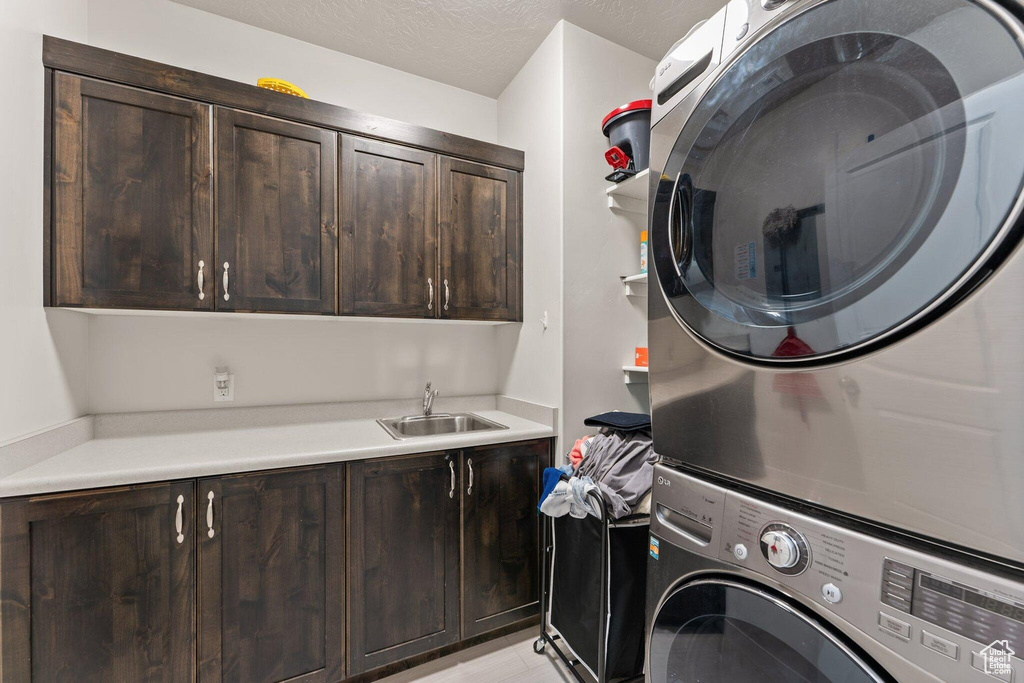 Clothes washing area with a textured ceiling, stacked washer / dryer, a sink, cabinet space, and indoor wet bar