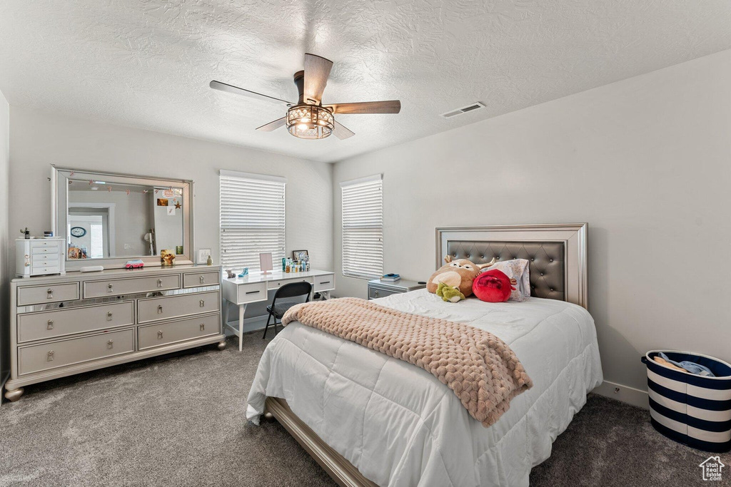 Carpeted bedroom with a textured ceiling, baseboards, ceiling fan, and visible vents