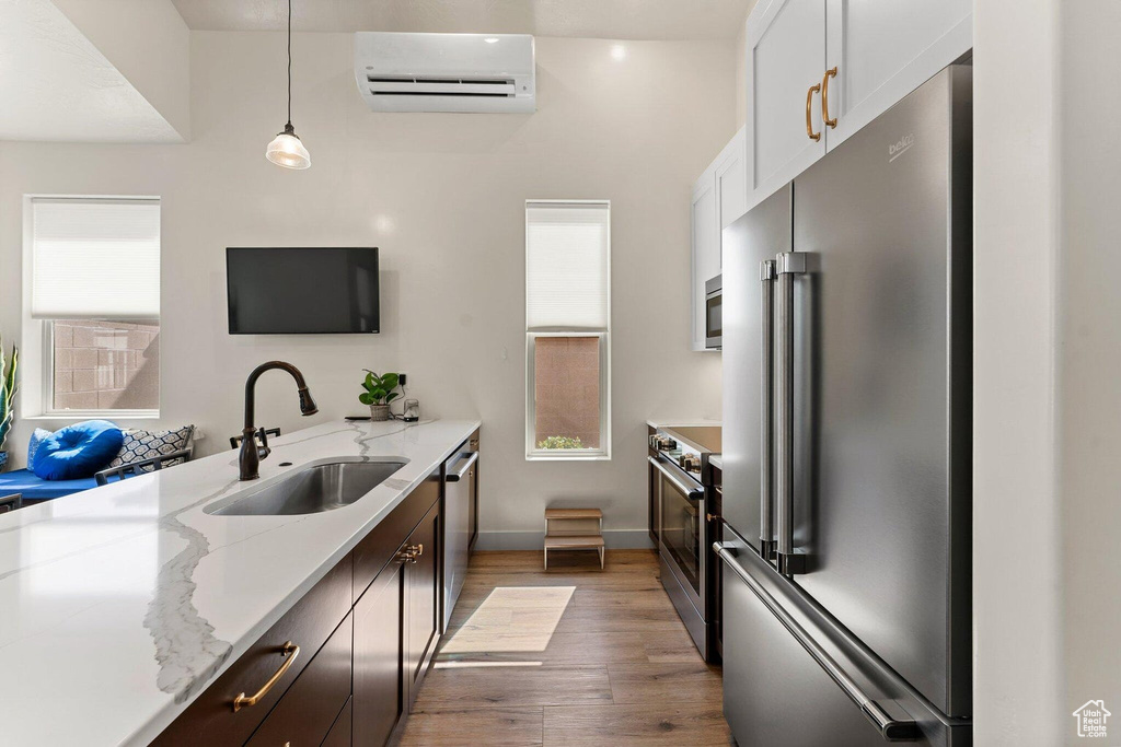 Kitchen with light wood-type flooring, a sink, light stone countertops, appliances with stainless steel finishes, and a wall mounted air conditioner