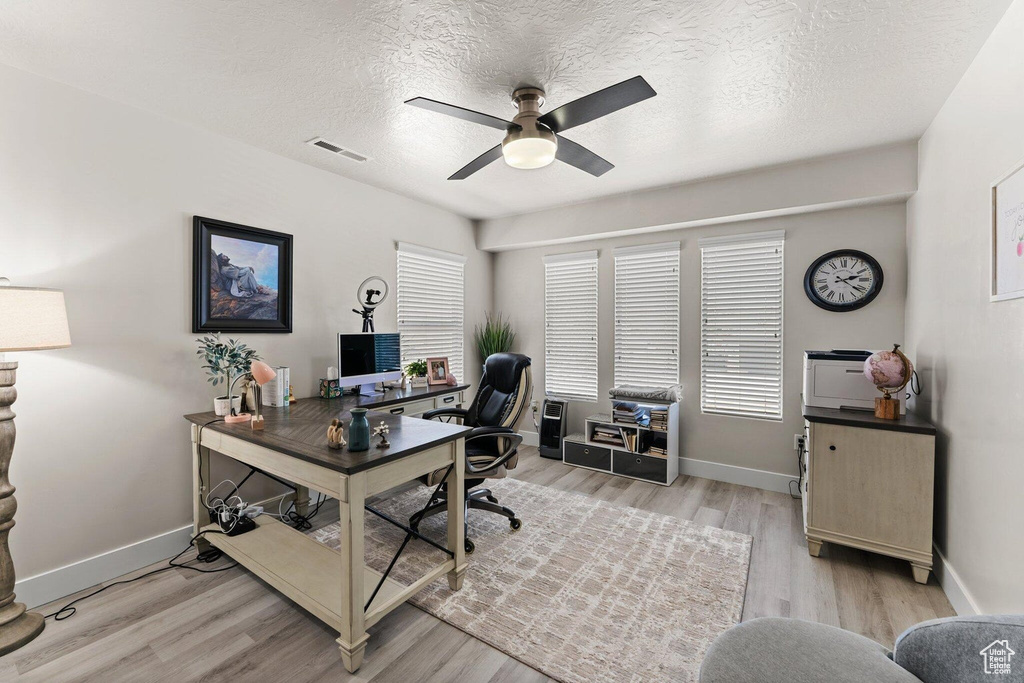 Home office with light wood finished floors, baseboards, ceiling fan, and visible vents