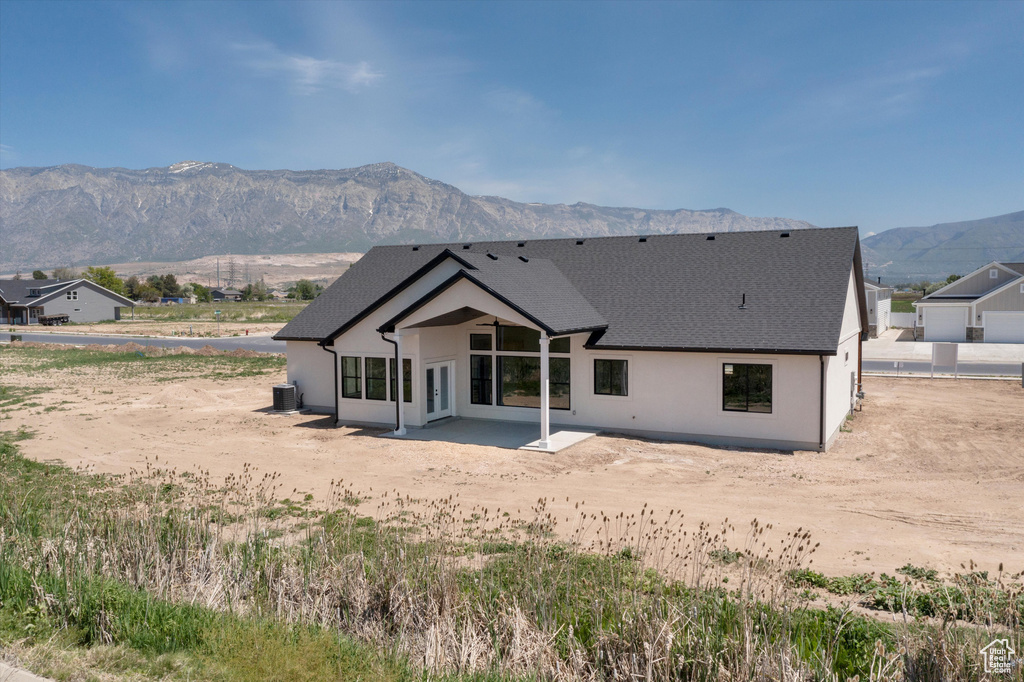 Back of property featuring a mountain view, stucco siding, a shingled roof, a patio, and central AC