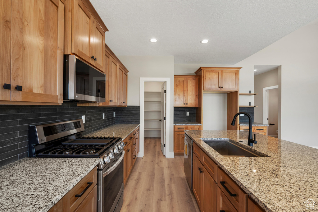 Kitchen featuring appliances with stainless steel finishes, a sink, light wood-style flooring, tasteful backsplash, and light stone countertops