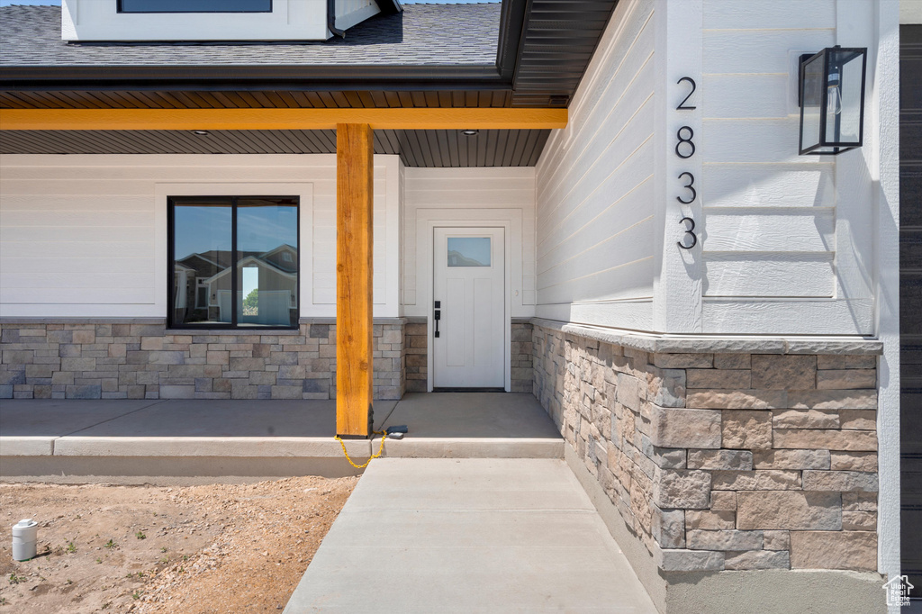 View of exterior entry featuring stone siding, a shingled roof, and a porch