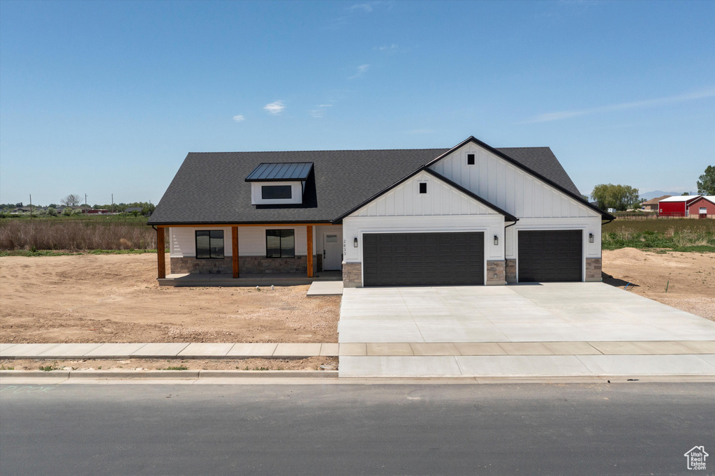 Modern inspired farmhouse with a garage, stone siding, driveway, board and batten siding, and a porch