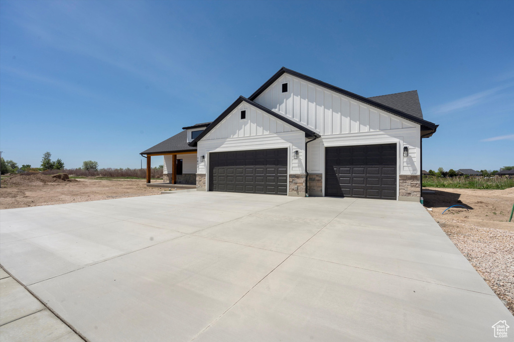 View of front of property with a garage, board and batten siding, stone siding, and driveway