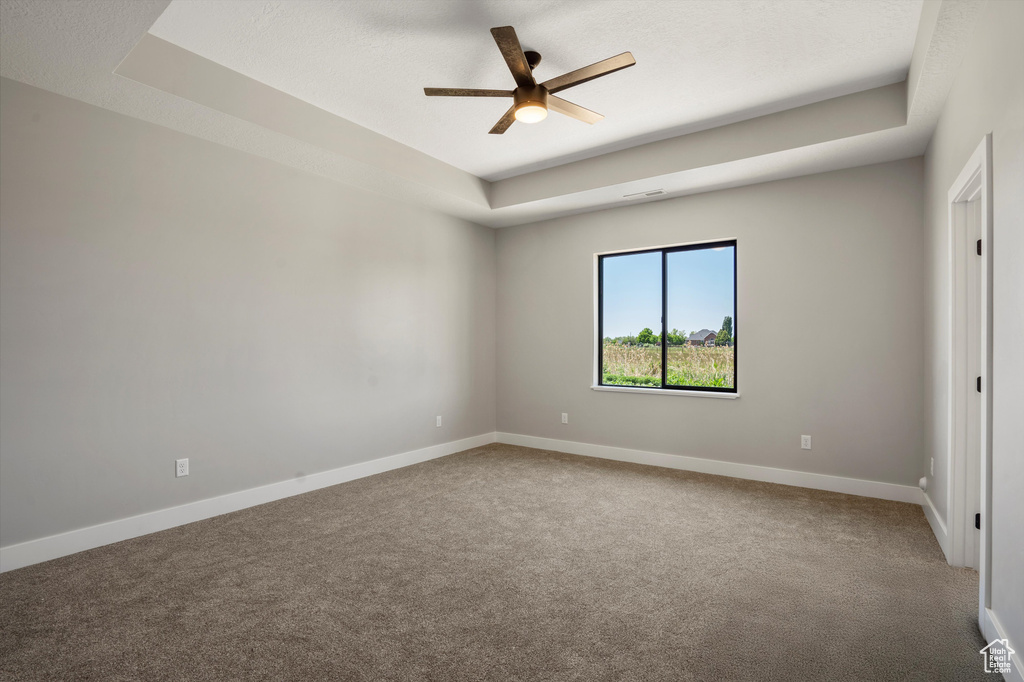 Carpeted spare room with a raised ceiling, ceiling fan, and baseboards