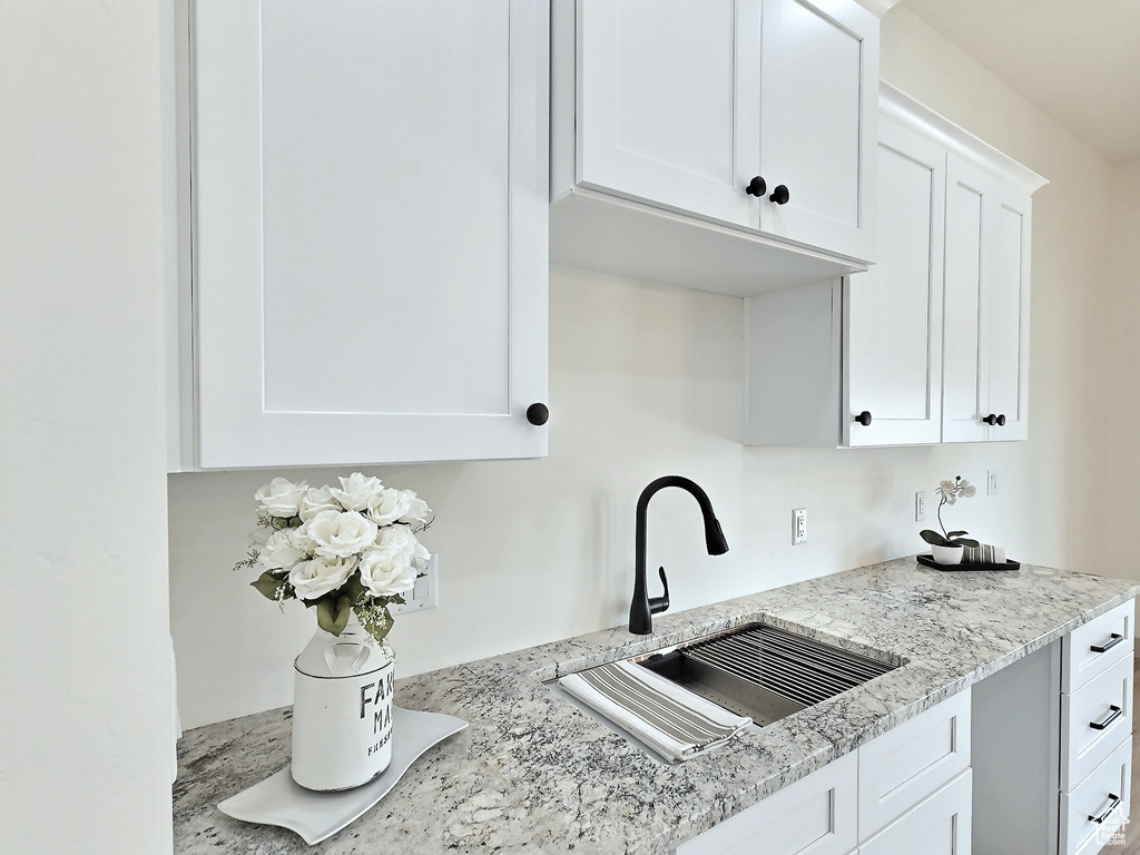Kitchen featuring white cabinets, a sink, and light stone countertops