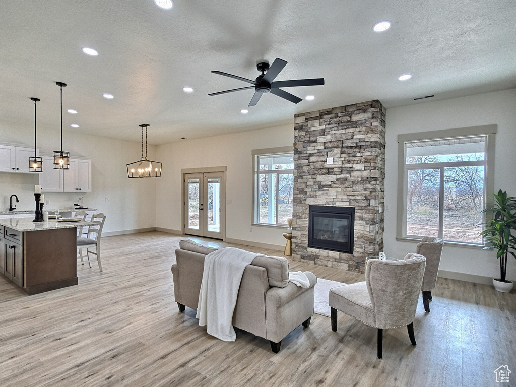 Living room with ceiling fan with notable chandelier, light wood-type flooring, a fireplace, and a textured ceiling