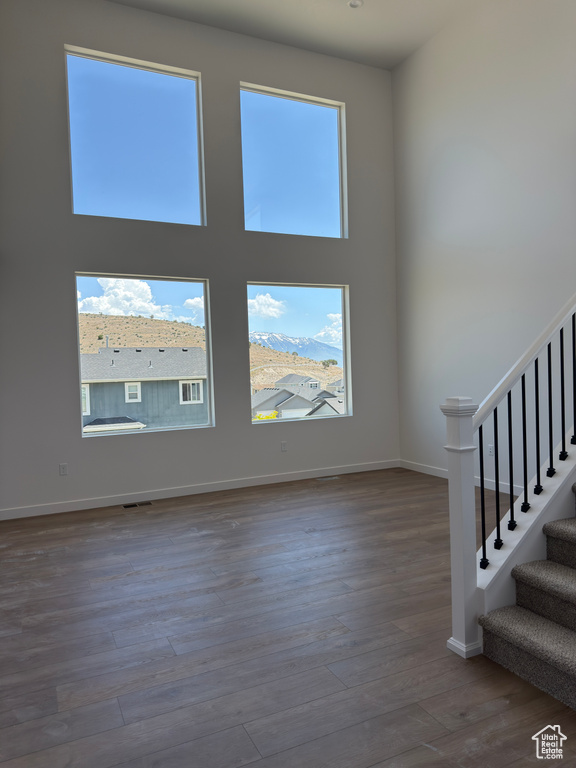 Empty room with wood finished floors, stairs, baseboards, and a high ceiling