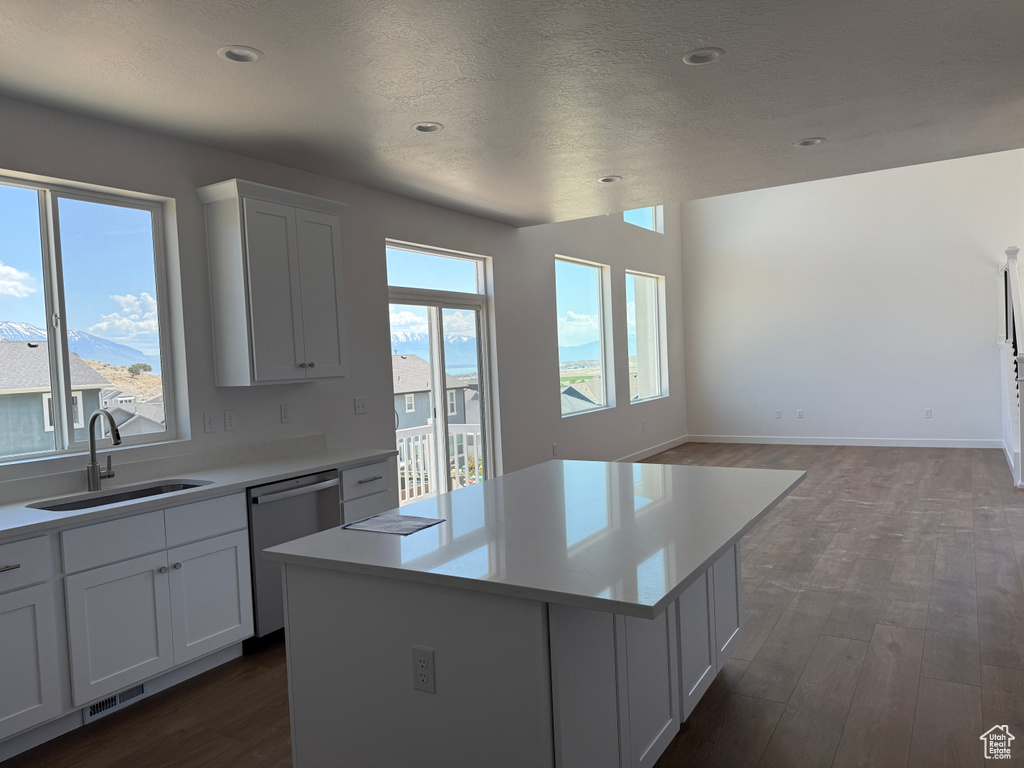 Kitchen with stainless steel dishwasher, a sink, dark wood-type flooring, light countertops, and a kitchen island