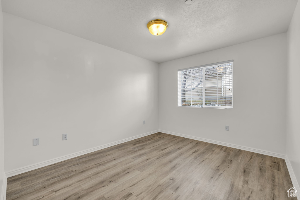 Empty room with a textured ceiling, baseboards, and wood finished floors