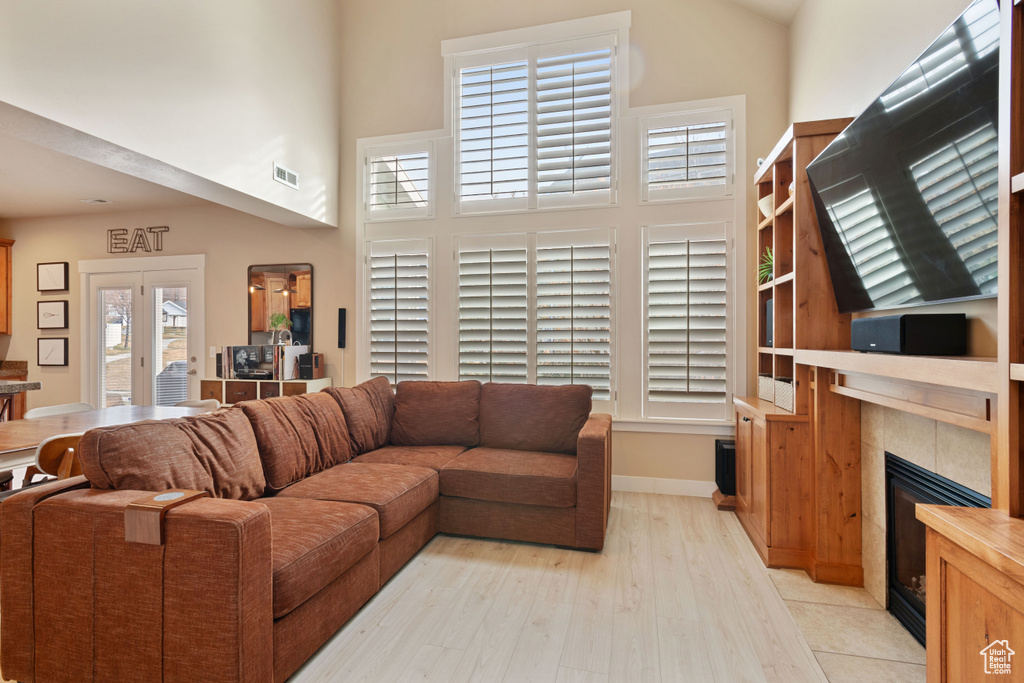 Living area with light wood-type flooring, baseboards, a high ceiling, visible vents, and a tiled fireplace