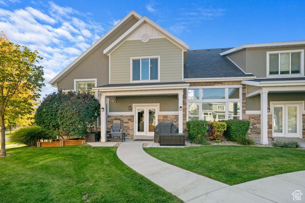 Back of property with stone siding, stucco siding, french doors, and a yard