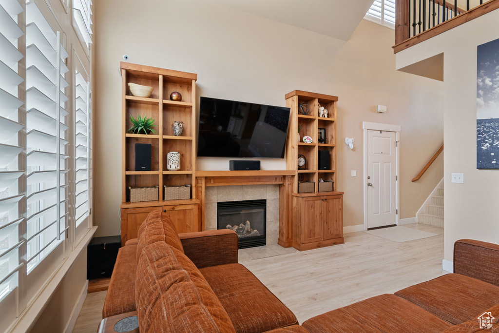 Living room featuring stairway, light wood-type flooring, baseboards, a towering ceiling, and a tile fireplace