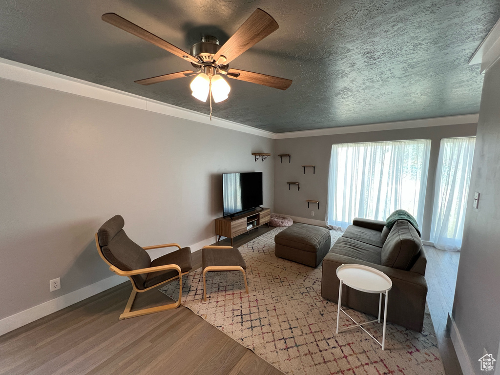 Living room featuring wood finished floors, baseboards, a ceiling fan, and a textured ceiling