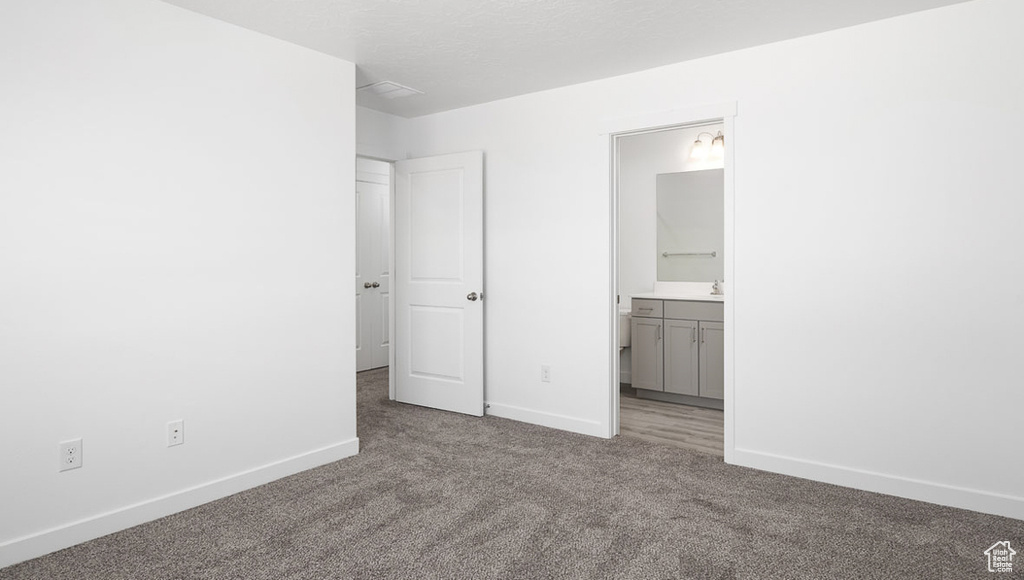 Unfurnished bedroom with ensuite bathroom, baseboards, carpet, and a textured ceiling