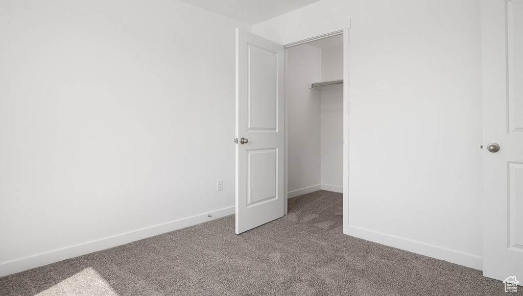 Unfurnished bedroom featuring baseboards, a walk in closet, a closet, and carpet flooring