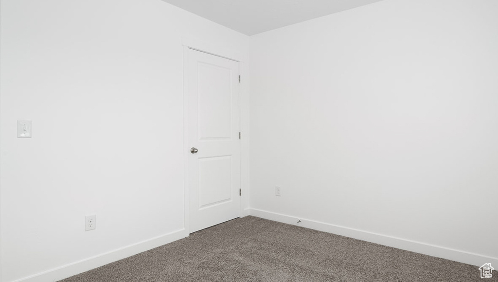 Spare room featuring baseboards and dark carpet