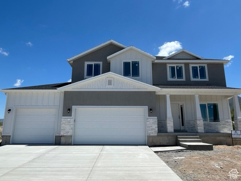 View of front of house featuring an attached garage, stone siding, board and batten siding, a porch, and driveway