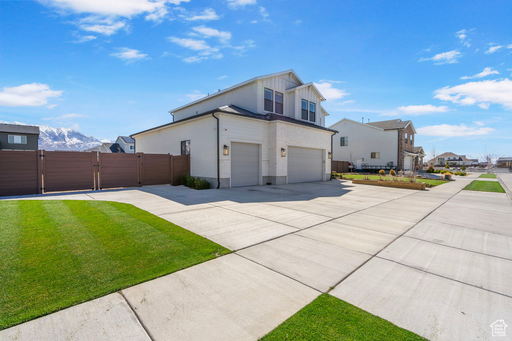 View of home's exterior with concrete driveway, an attached garage, board and batten siding, a gate, and a yard