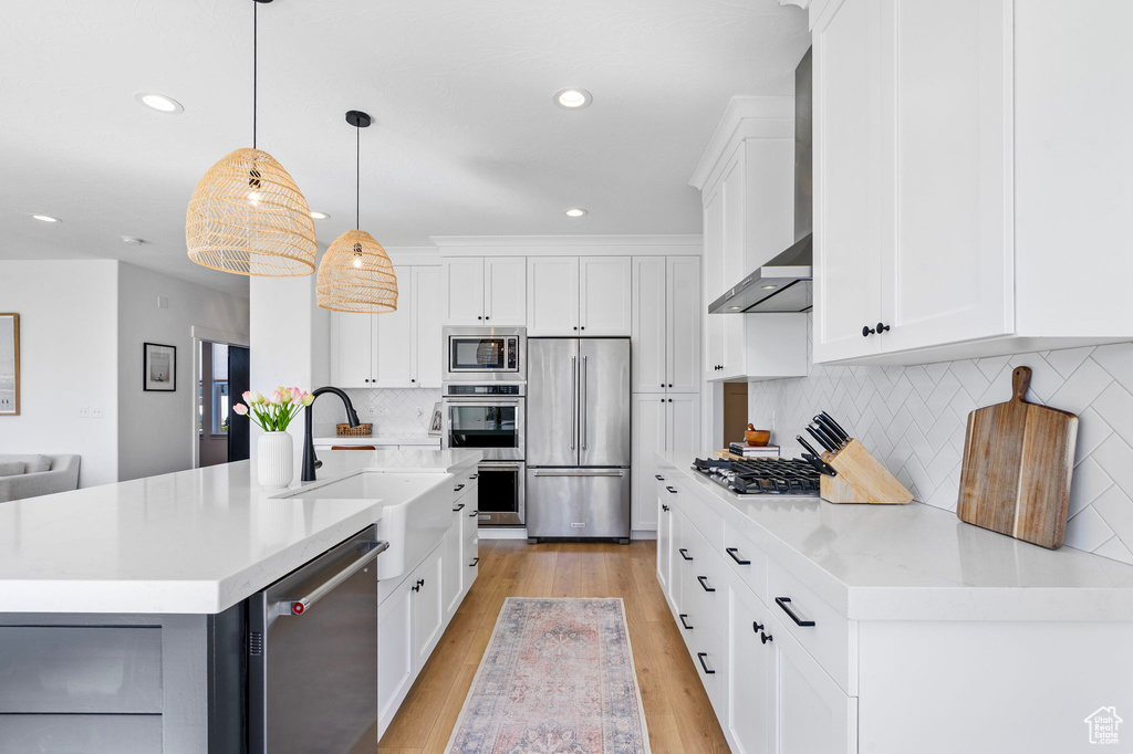 Kitchen with white cabinetry, a sink, light wood-style flooring, appliances with stainless steel finishes, and wall chimney exhaust hood