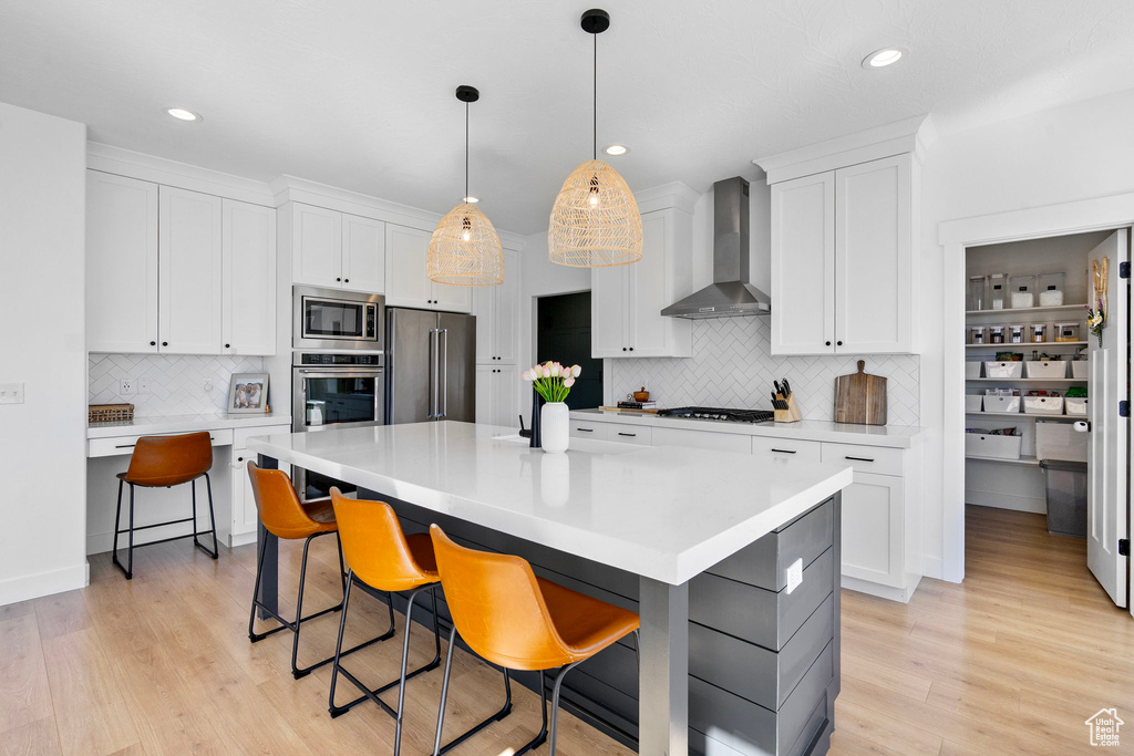 Kitchen with light wood finished floors, wall chimney exhaust hood, light countertops, and stainless steel appliances