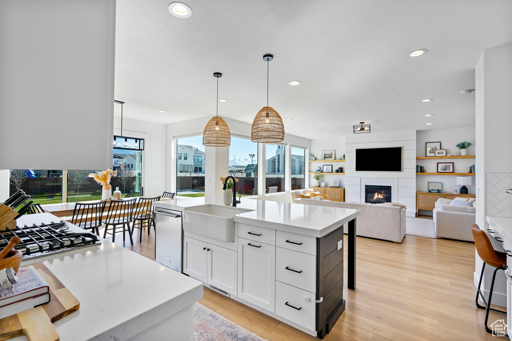 Kitchen featuring light countertops, a sink, a large fireplace, dishwasher, and light wood-style flooring
