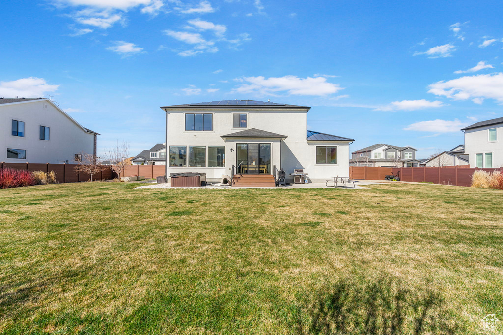 Rear view of house with a fenced backyard, solar panels, a hot tub, and a patio
