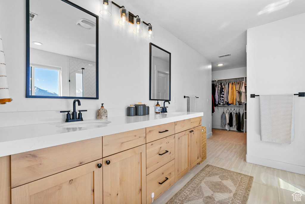 Bathroom featuring a walk in closet, double vanity, visible vents, and a sink