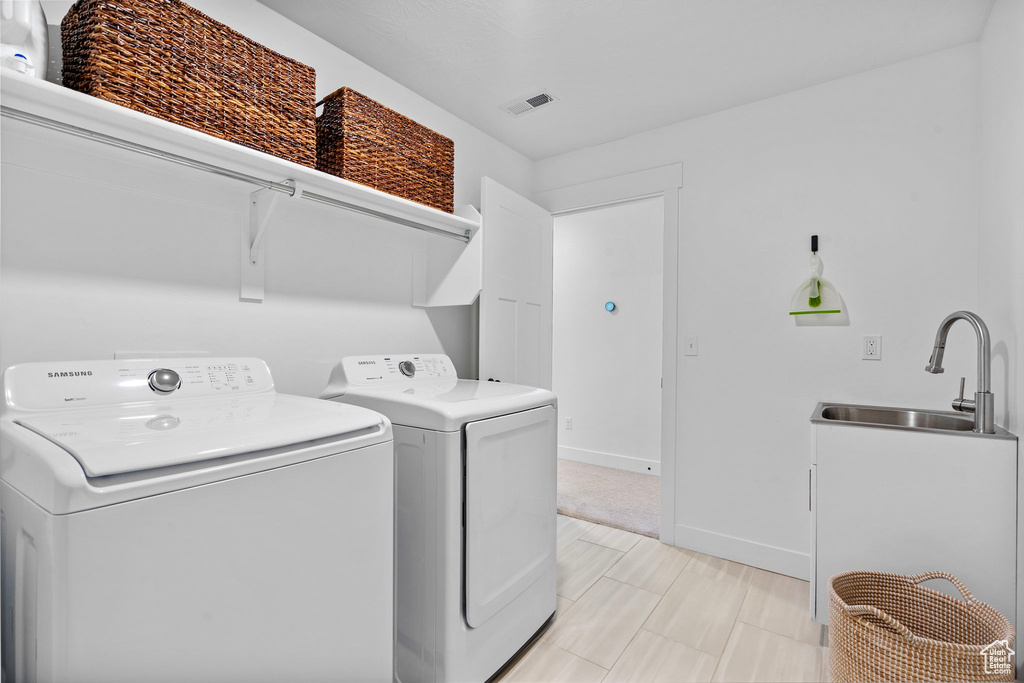 Washroom featuring independent washer and dryer, baseboards, a sink, visible vents, and laundry area