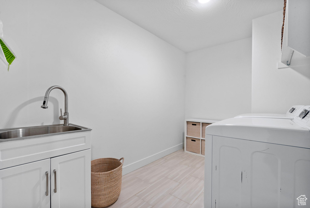 Clothes washing area featuring light wood finished floors, baseboards, a sink, cabinet space, and separate washer and dryer