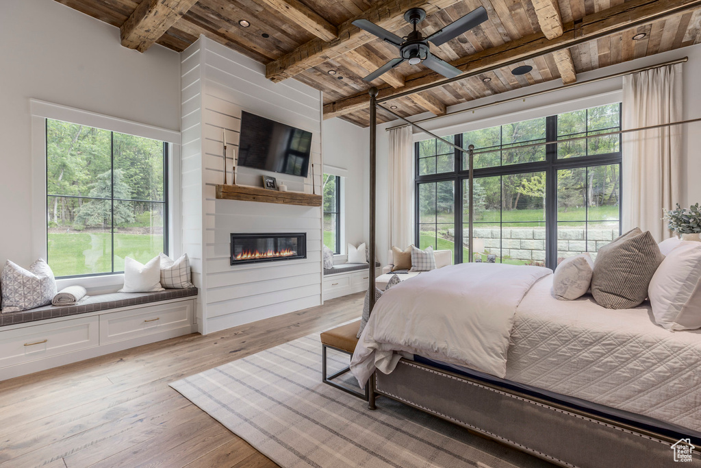 Bedroom with wooden ceiling with exposed beams, light wood-type flooring, and a large fireplace