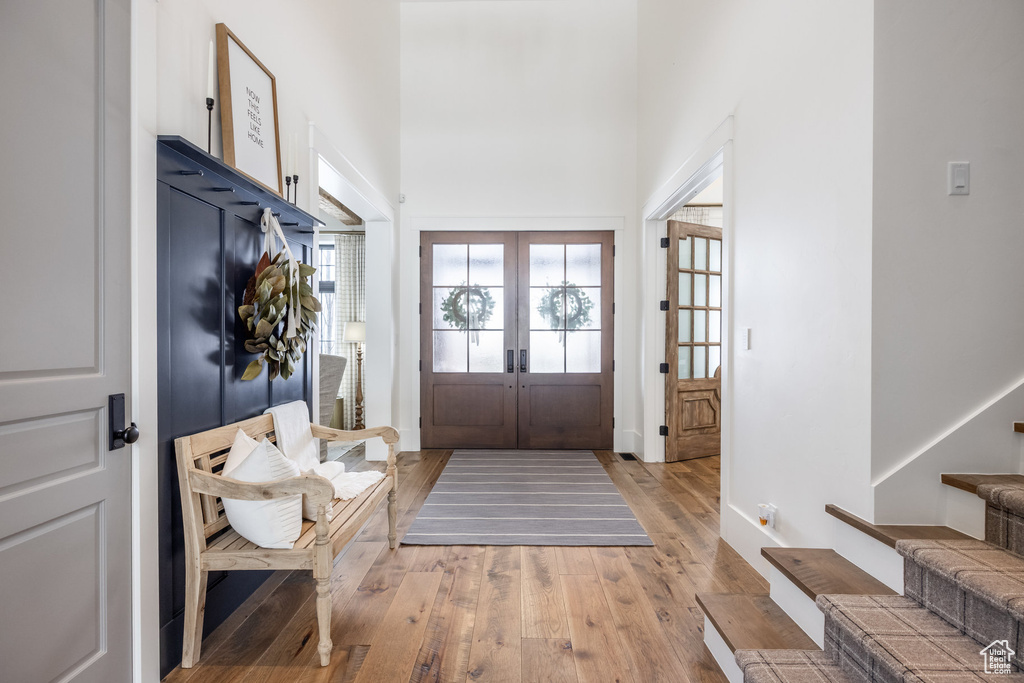 Foyer with french doors, light wood-style floors, a towering ceiling, stairs, and baseboards