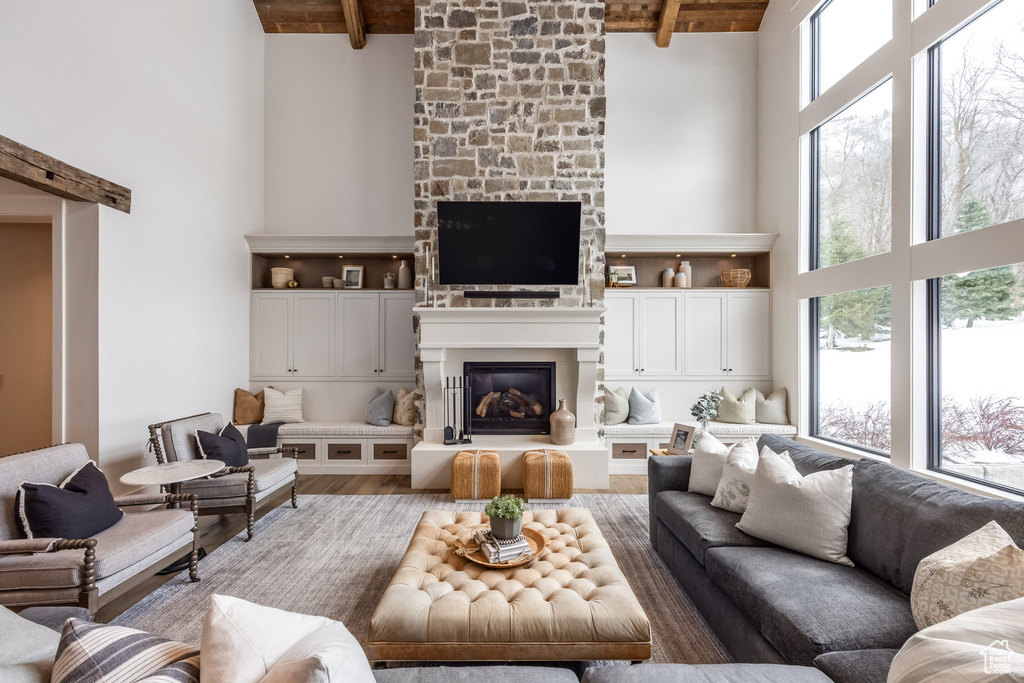 Living area featuring a towering ceiling, a large fireplace, wooden ceiling with exposed beams, and wood finished floors